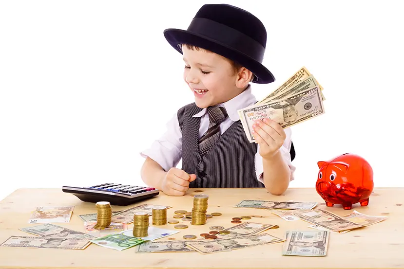 Little boy in black hat and tie at the table counts money, isolated on white;