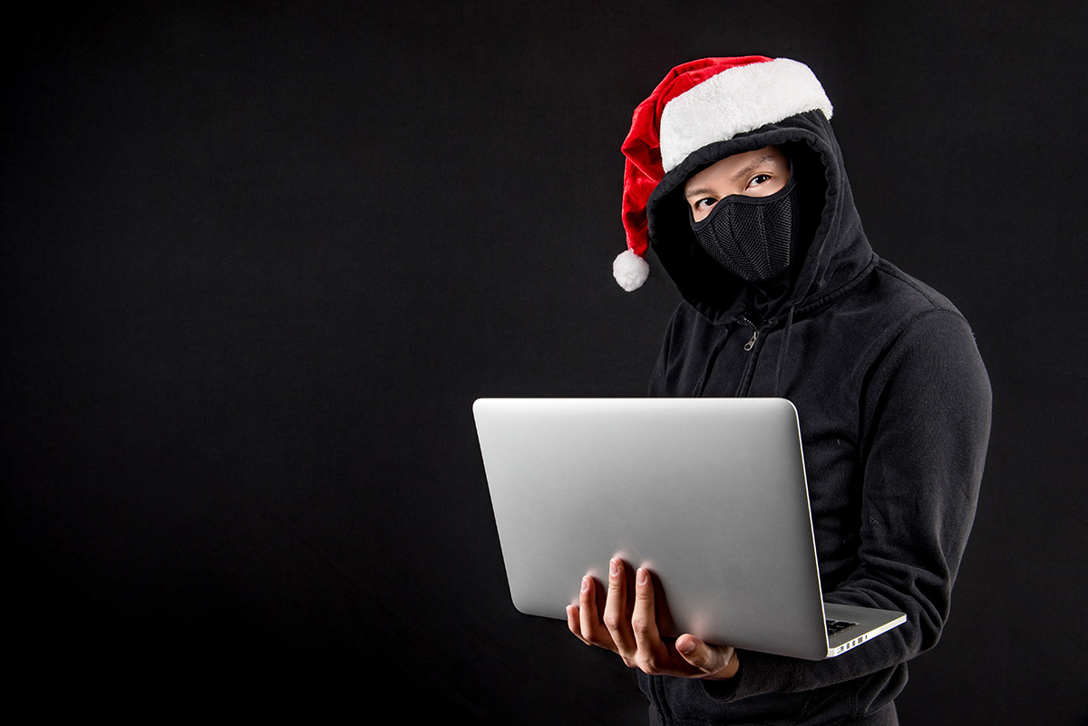 Mysterious male santa hacker holding laptop computer, anonymous man on black background, ransomware cyber attack and internet security on